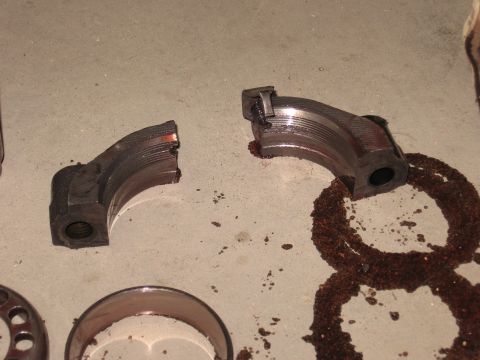 1977 Ford F-150 - Damaged engine bearing caps and a rusty oil ring are shown on a concrete surface.