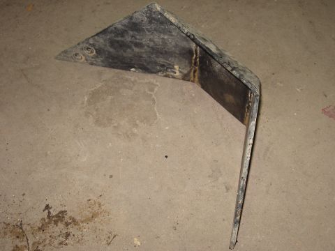 1977 Ford F-150 - A bent metal part with visible welds and indentations sits on a concrete floor.