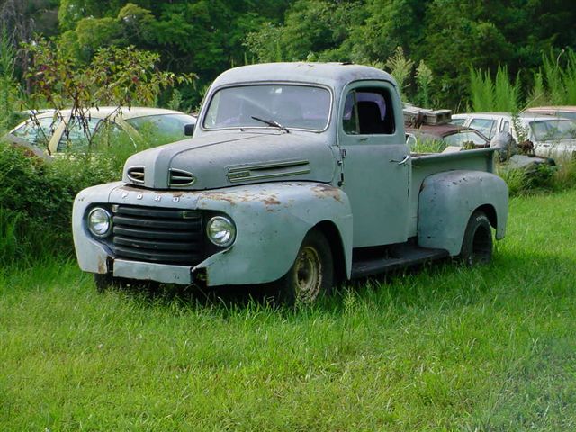 Gray 1948 Ford F-series pickup truck parked in grass with other vehicles in background