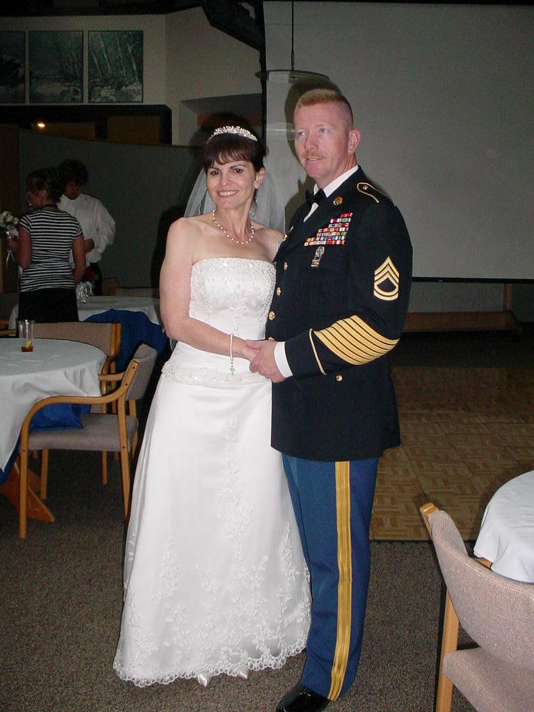 Bride in white dress and groom in military uniform holding hands indoors