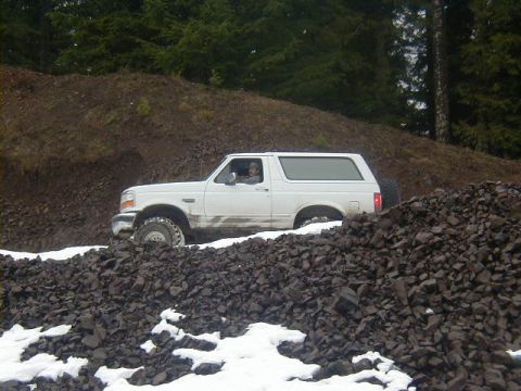 1994 Ford Explorer - A white Ford Bronco navigates a rough, off-road path covered in rocks and patches of snow.