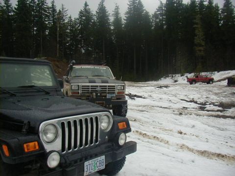 1994 Ford Explorer - Two off-road vehicles parked in a snowy forest clearing with a red pickup truck in the distance.