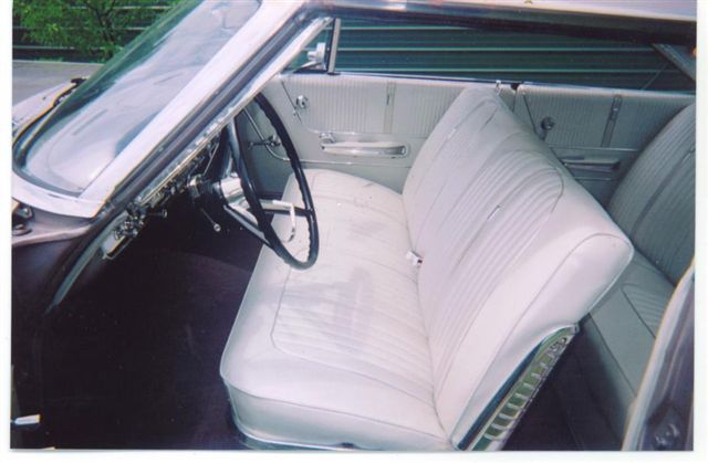 Car interior with white vinyl seats, black steering wheel, and chrome accents