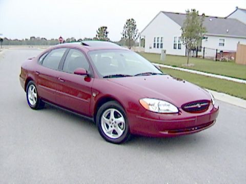 2002 Ford Taurus - A red 2002 Ford Taurus is parked on a street in front of a house.