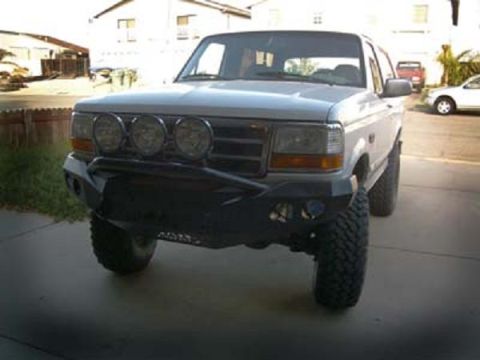 1991 Ford Bronco - This white SUV features an aftermarket bumper and multiple spotlights, seen from a 3/4 front angle.