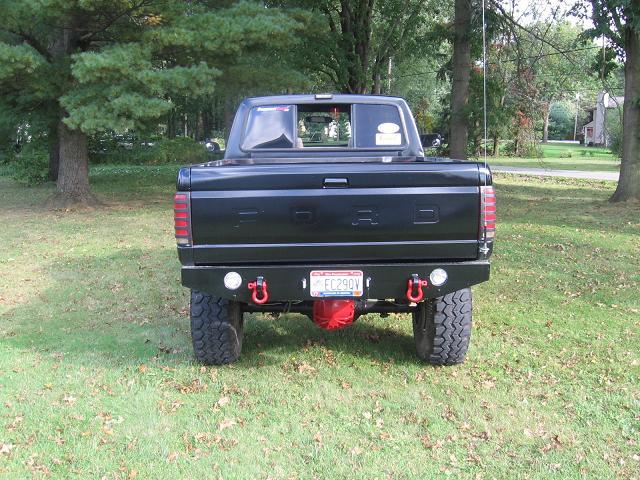 Rear view of lifted black Ford pickup on grass with custom bumper and red shackles