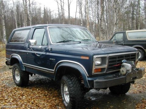 1991 Ford Bronco - A dark blue Ford Bronco is parked in a wooded area next to another Bronco.