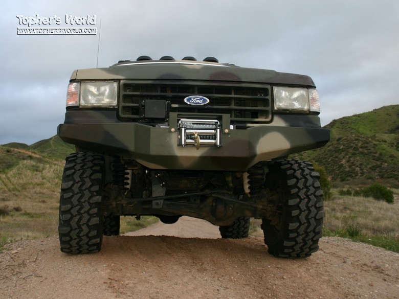 Front view of camouflage lifted Ford SUV with winch bumper and off-road tires on dirt trail