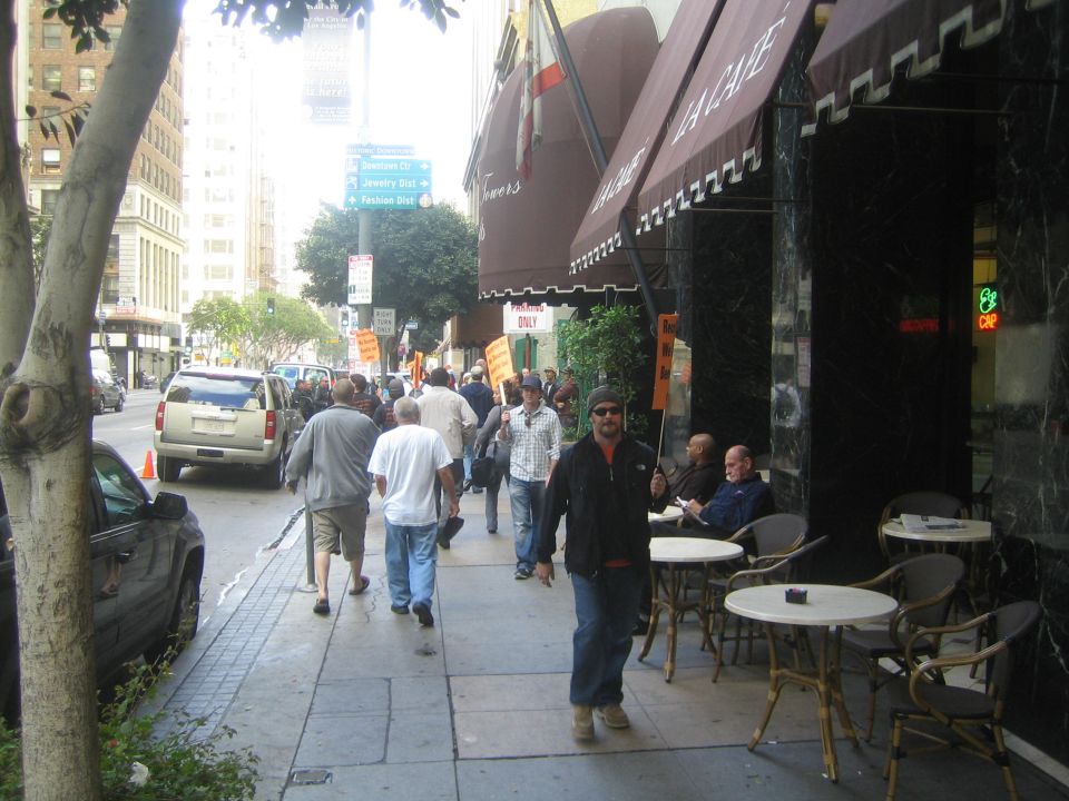 People walking on a downtown city sidewalk past a cafe with outdoor tables