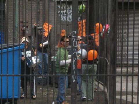 1990 Ford Bronco - group of protesters holding orange picket signs and beating a drum gathers behind a black metal gate.
