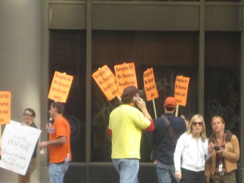1990 Ford Bronco - Protesters hold orange signs reading Recognize Us, We Deserve Benefits Too in front of a darkened storefront.