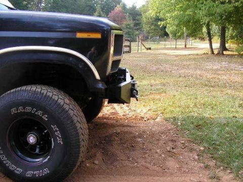 1991 Ford Bronco - A black Ford Bronco is parked on a dirt road with grass and trees in the background.