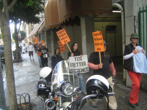 1990 Ford Bronco - Picketers carry orange signs and a You Better Recognize placard along a sidewalk beside a parked police motorcycle.