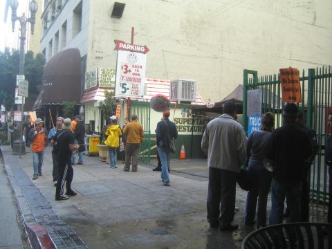 1990 Ford Bronco - group of people gathered on a damp downtown sidewalk beside a Parking rate sign and a Mexican restaurant storefront.