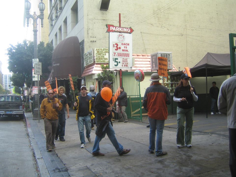People walking on a city sidewalk carrying orange balloons by a parking sign