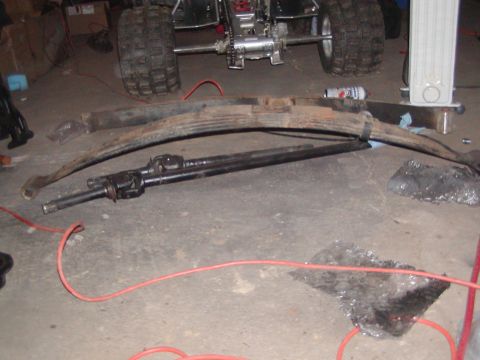 1991 Ford Bronco - Vehicle parts, including leaf springs and a driveshaft, are laid out on a garage floor.