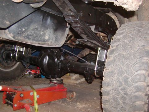1991 Ford Bronco - The underside of a vehicle shows the rear axle, leaf springs, and fuel tank, with a jack supporting the axle.