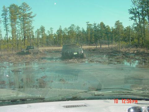 1995 Dodge 1500 - Two trucks are stuck in the mud in a wooded area, with one vehicle significantly submerged.