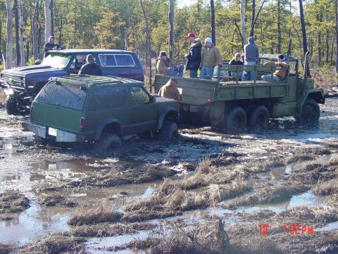 1995 Dodge 1500 - Multiple vehicles are bogged down in a muddy, wooded terrain, with several people observing the scene.
