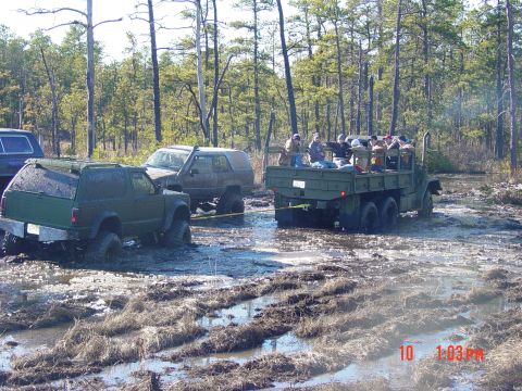 1995 Dodge 1500 - Several off-road vehicles are stuck in the mud with people riding in the back of a military truck.