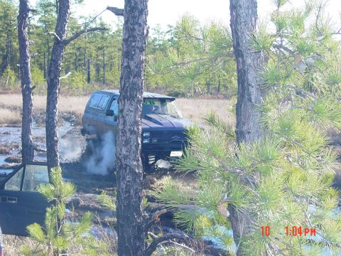 1995 Dodge 1500 - A dark blue SUV navigates through a muddy, wooded area, with its front passenger door ajar.
