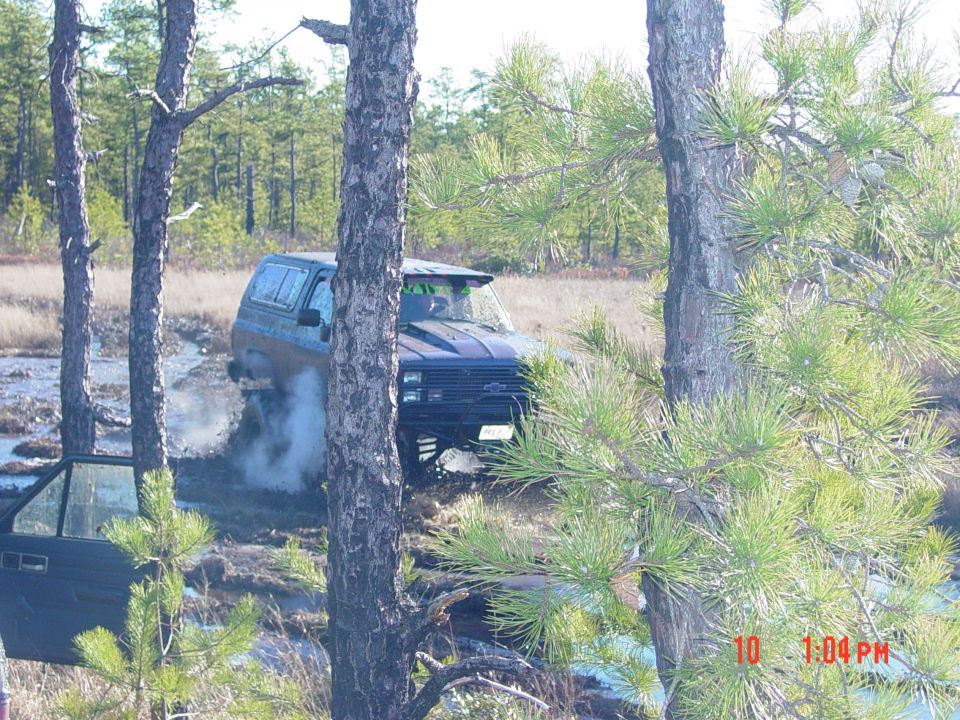 Dark blue SUV with aftermarket hood scoop stuck in mud, front passenger door open