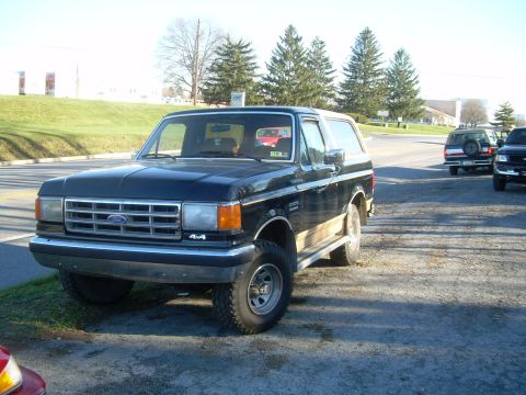 1992 Ford Bronco - This black 1992 Ford Bronco features distinctive wood paneling and is seen parked near a road with other vehicles in the background.