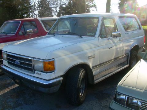 1992 Ford Bronco - A white 1992 Ford Bronco is seen from a 3/4 front angle, parked outdoors with other vehicles.
