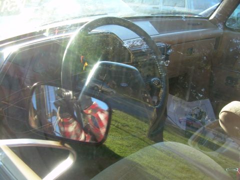 1992 Ford Bronco - The interior of a 1992 Ford Bronco shows a brown dashboard and steering wheel, with a side mirror reflecting a person.