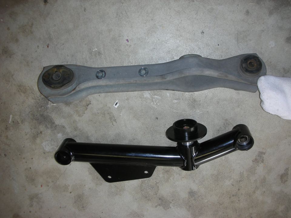 Two car suspension control arms, one gray and one black, on a concrete floor