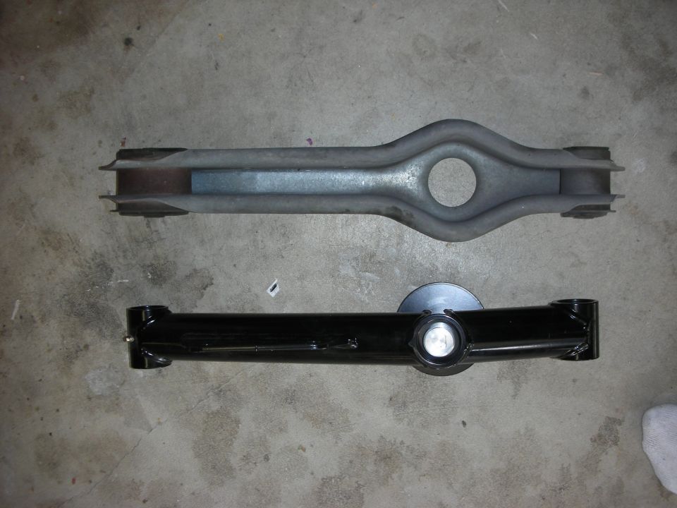 Two suspension control arms, one old and one new, on a concrete floor
