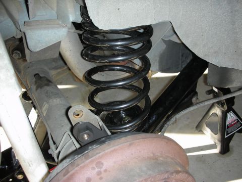 1990 Ford Mustang - Under-car view of a rear suspension on jack stands, showing a black coil spring seated on the rear axle, a shock absorber, control-arm brac…