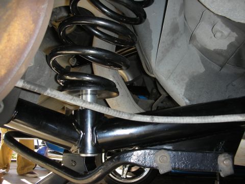 1990 Ford Mustang - The underside of a vehicle shows its rear suspension system, including a coil spring and various metal linkages.