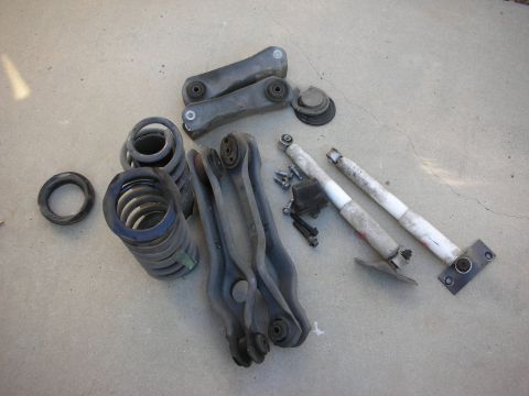 1990 Ford Mustang - Collection of automotive suspension parts, likely for a rear-wheel-drive car, on a concrete surface.