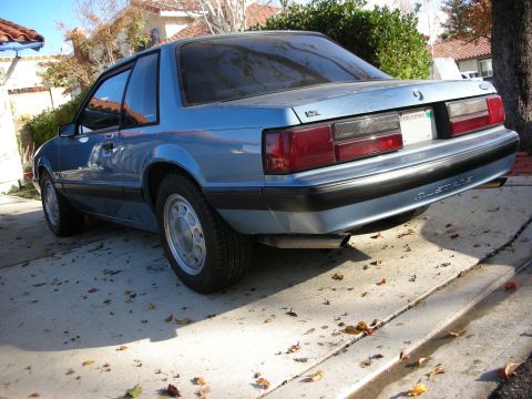 1990 Ford Mustang - The rear quarter panel of a blue coupe shows the 'Mustang' script on the bumper trim.