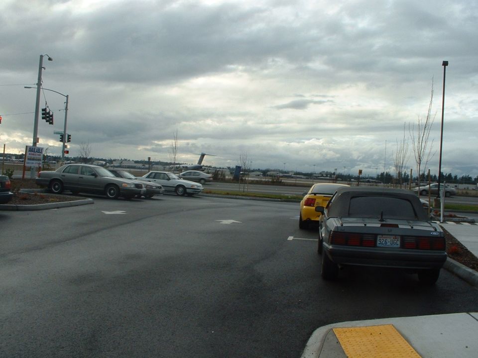 Dark gray convertible Mustang parked in a lot, yellow Mustang behind it, and sedans in background