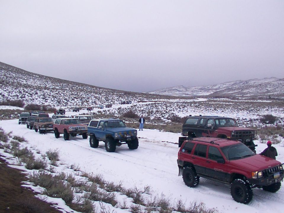 Line of off-road vehicles on a snowy road, with a red Jeep Grand Cherokee in the foreground