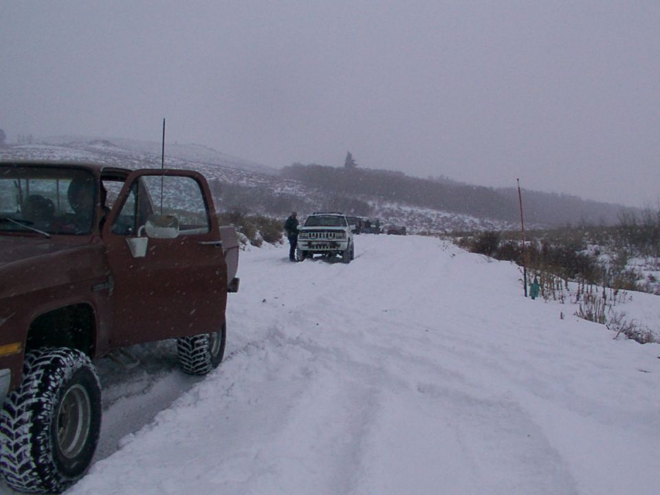 Brown truck in foreground, white SUV and another truck in background on snowy road