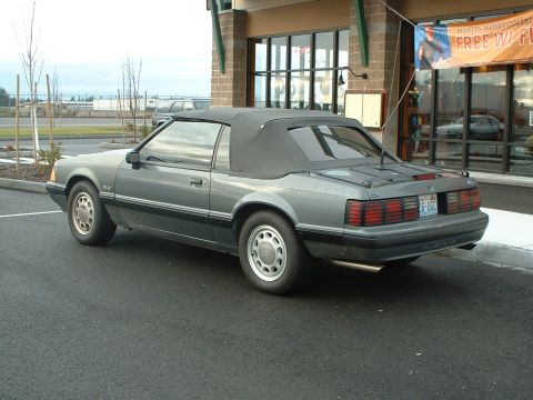 2000 Ford Crown Victoria - A gray 1987 Ford Mustang convertible is parked in front of a building with a "Free Wi-Fi" sign.