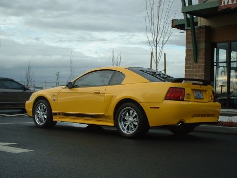 2000 Ford Crown Victoria - A yellow Ford Mustang is parked outside a building, with another vehicle visible in the background.