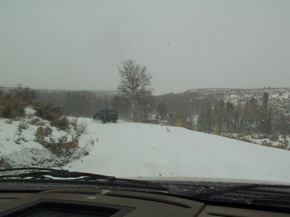 Dark SUV driving on a snow-covered road with trees and hills in the background