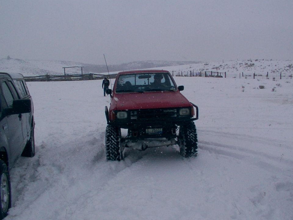 red Toyota pickup with big tires driving in snow, another SUV next to it