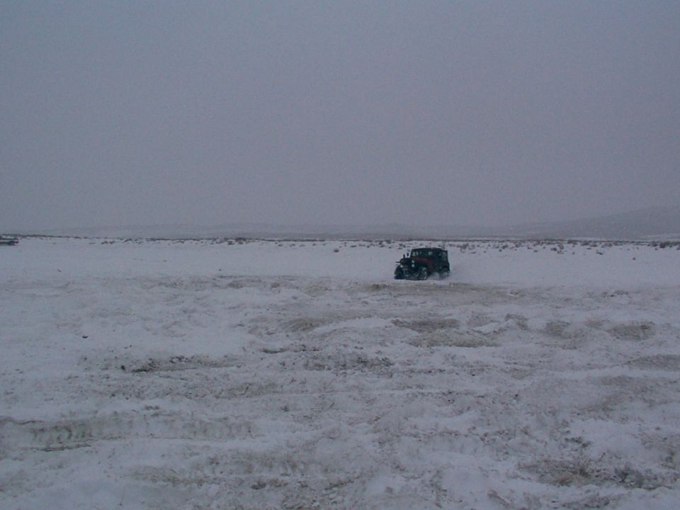 Dark SUV driving through snow, low angle, overcast sky