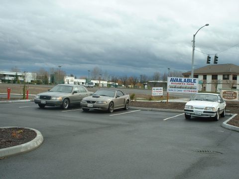 2000 Ford Crown Victoria - Three cars are parked in a lot under a cloudy sky, with buildings and signs in the background.