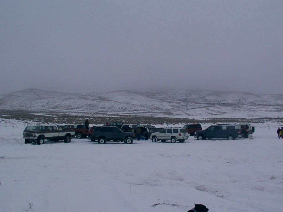 Several SUVs and trucks parked in a snowy field under a cloudy sky