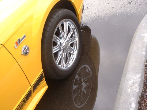 2000 Ford Crown Victoria - Close-up of a yellow car's fender and wheel, showing a reflection in wet pavement.
