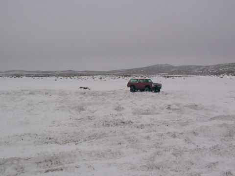 2003 Ford Ranger - A red SUV is being towed across a snowy landscape with distant hills under a cloudy sky.