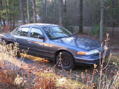1991 Ford LTD Crown Victoria - A blue sedan, likely a 1992 model, sits parked on a dirt road surrounded by trees and dry vegetation.