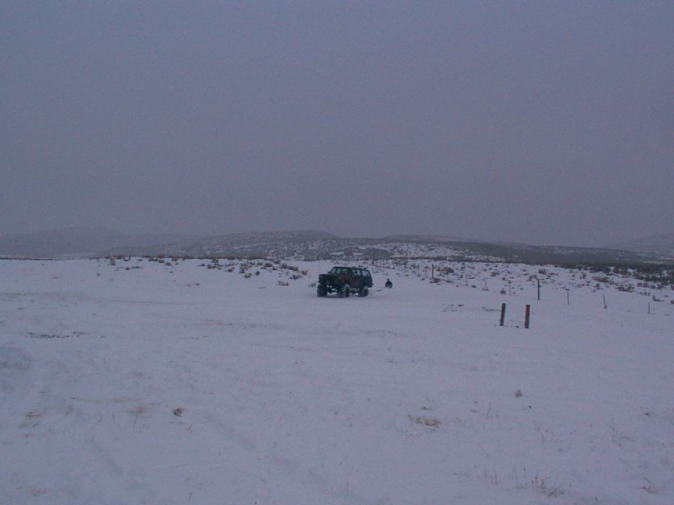 Off-road vehicle parked in a snowy field with hills in the background