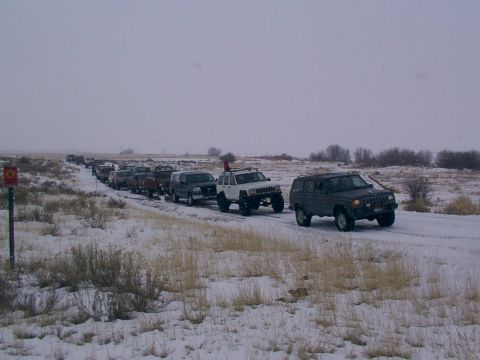 2003 Ford Ranger - Multiple SUVs and trucks drive in a convoy on a snow-covered road under a cloudy sky.